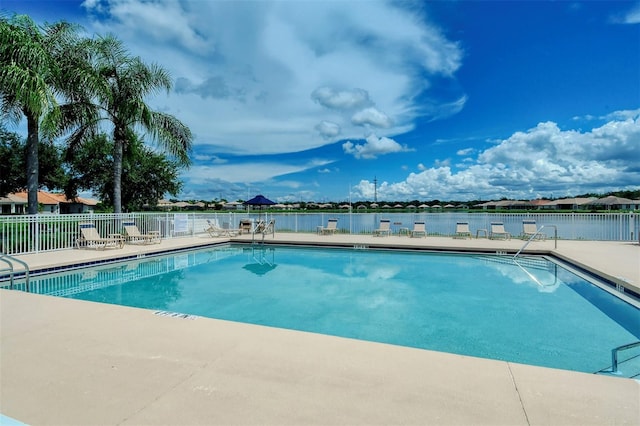 community pool with a patio area, fence, and a water view