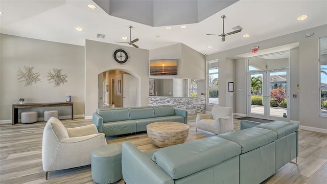 living room with french doors, a towering ceiling, ceiling fan, and light hardwood / wood-style floors