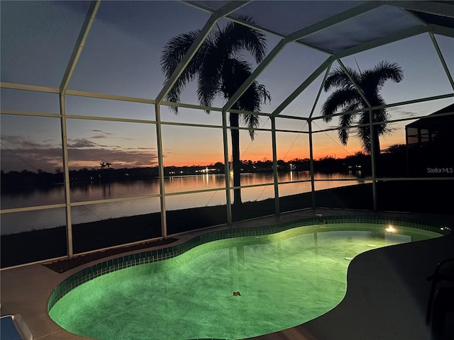 pool at dusk with glass enclosure, a patio, a water view, and an outdoor pool