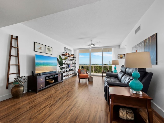 living room featuring wood-type flooring, a textured ceiling, ceiling fan, and a wall of windows