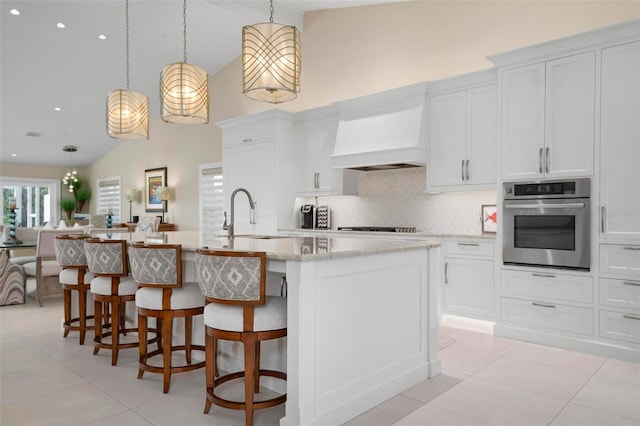 kitchen featuring sink, stainless steel oven, decorative light fixtures, custom range hood, and a kitchen island with sink