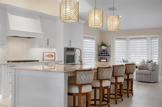 kitchen with premium range hood, pendant lighting, stainless steel appliances, a kitchen island with sink, and white cabinets