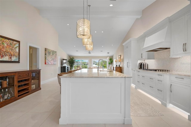 kitchen featuring sink, decorative light fixtures, light stone countertops, a kitchen island with sink, and white cabinets