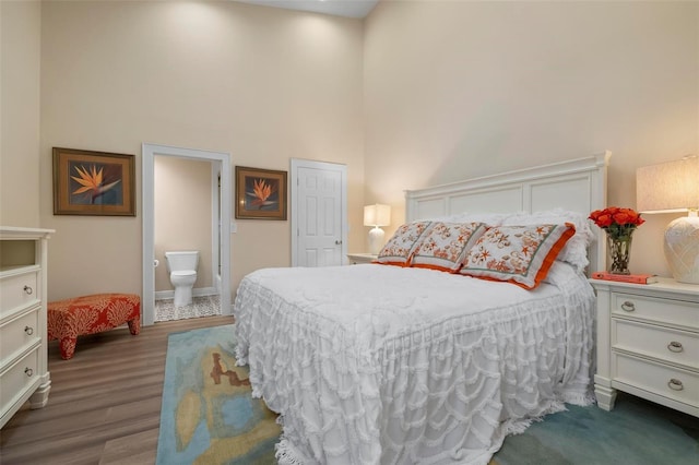 bedroom with dark wood-type flooring, a towering ceiling, and ensuite bath