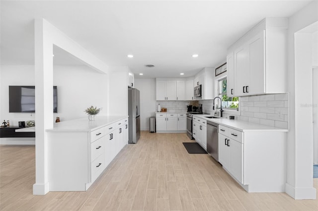 kitchen with sink, appliances with stainless steel finishes, white cabinetry, light hardwood / wood-style floors, and decorative backsplash