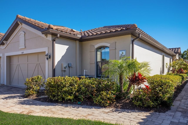 view of front of property with a garage, a tile roof, decorative driveway, and stucco siding