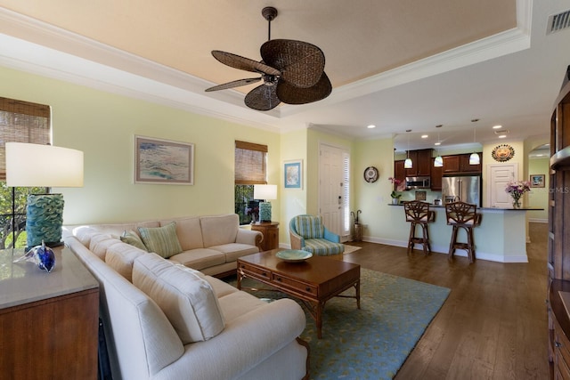 living area featuring dark wood-style flooring, recessed lighting, a raised ceiling, ornamental molding, and baseboards