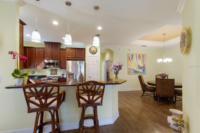 kitchen with arched walkways, decorative light fixtures, a breakfast bar area, dark countertops, and appliances with stainless steel finishes