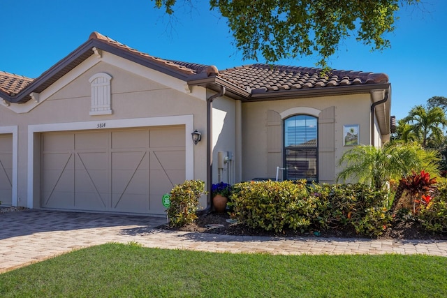 mediterranean / spanish home with a garage, a tiled roof, decorative driveway, a front lawn, and stucco siding