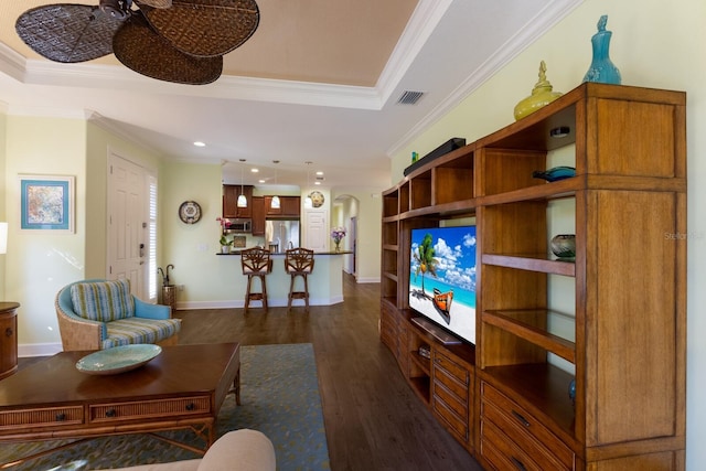 living room featuring arched walkways, dark wood-type flooring, visible vents, a raised ceiling, and crown molding