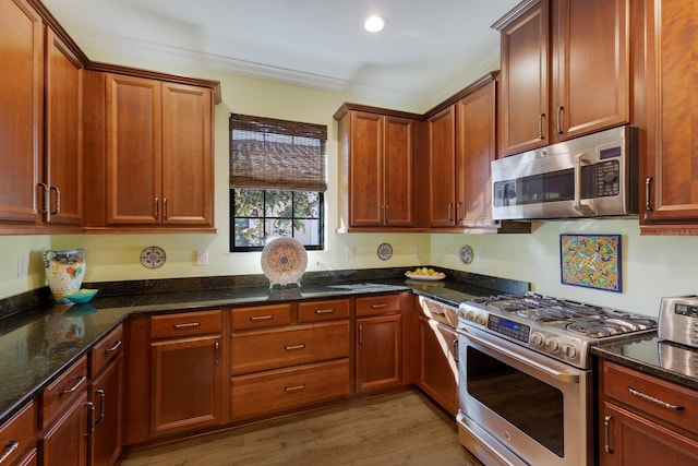 kitchen with stainless steel appliances, light wood-type flooring, dark stone countertops, and brown cabinetry