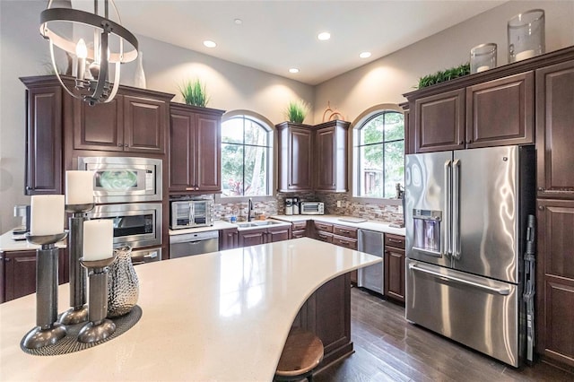 kitchen featuring pendant lighting, light countertops, backsplash, appliances with stainless steel finishes, and a sink