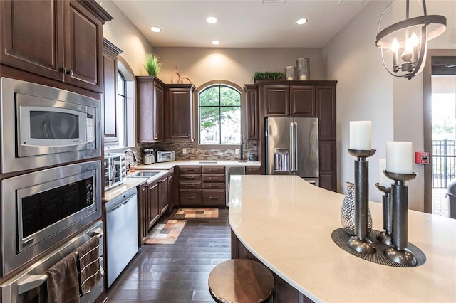 kitchen featuring backsplash, an inviting chandelier, stainless steel appliances, pendant lighting, and a sink