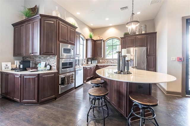 kitchen with stainless steel appliances, visible vents, light countertops, dark brown cabinets, and decorative light fixtures