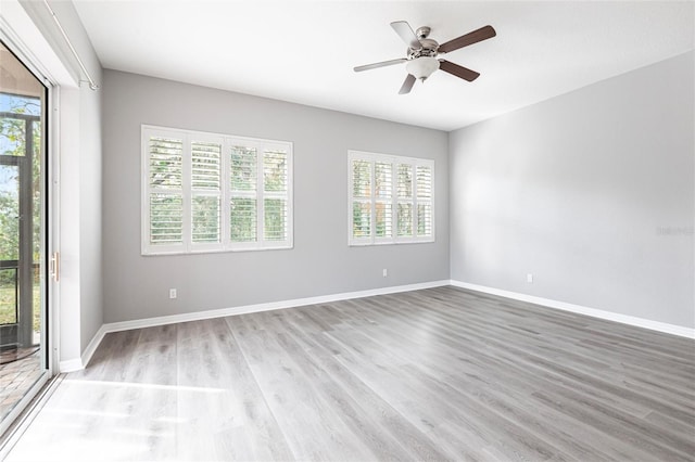 empty room featuring a healthy amount of sunlight, light wood-style flooring, baseboards, and ceiling fan