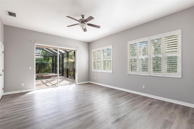 empty room with a sunroom, visible vents, ceiling fan, and wood finished floors