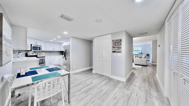 kitchen featuring appliances with stainless steel finishes, white cabinetry, decorative backsplash, light hardwood / wood-style floors, and a textured ceiling