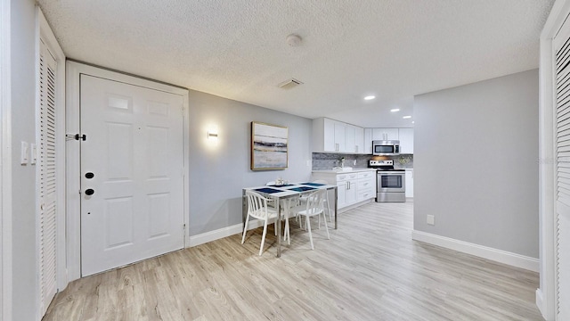 kitchen with white cabinetry, a textured ceiling, stainless steel appliances, light hardwood / wood-style floors, and backsplash