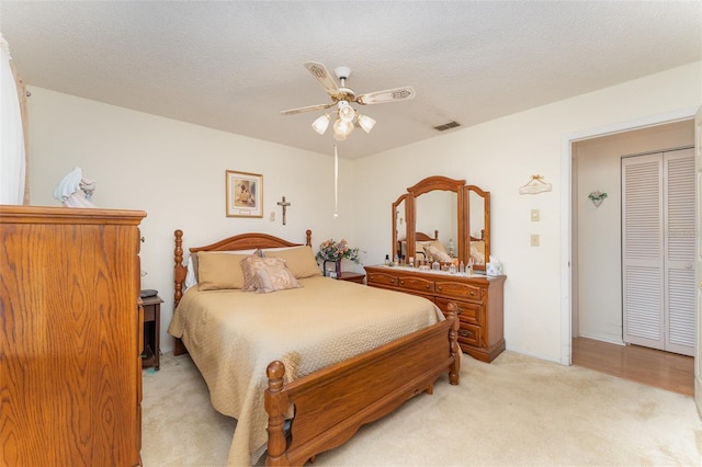 bedroom with ceiling fan, light carpet, and a textured ceiling