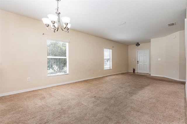 carpeted empty room with baseboards, visible vents, and an inviting chandelier