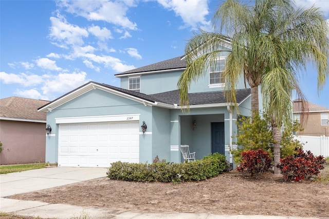 traditional home with driveway, a shingled roof, an attached garage, fence, and stucco siding