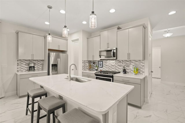 kitchen featuring sink, a breakfast bar area, appliances with stainless steel finishes, a kitchen island with sink, and decorative light fixtures