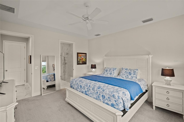 carpeted bedroom featuring a raised ceiling, ensuite bathroom, and ceiling fan