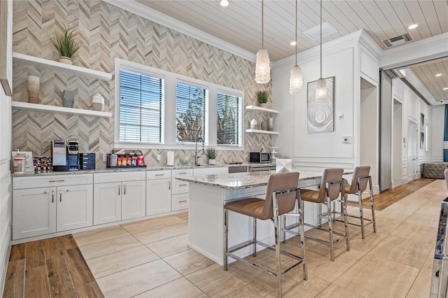 kitchen with ornamental molding, light stone countertops, pendant lighting, and white cabinets