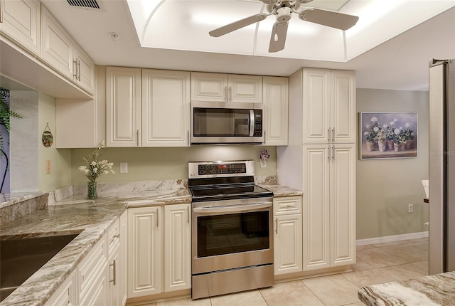 kitchen with a raised ceiling, light stone countertops, appliances with stainless steel finishes, and light tile patterned flooring