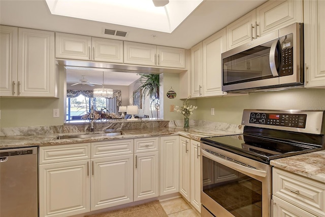 kitchen with light tile patterned flooring, sink, stainless steel appliances, light stone countertops, and ceiling fan with notable chandelier