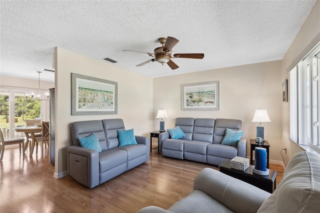 living room featuring ceiling fan with notable chandelier, wood-type flooring, and a textured ceiling