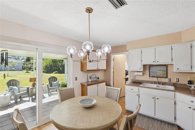 dining room featuring sink, a chandelier, a textured ceiling, and light wood-type flooring