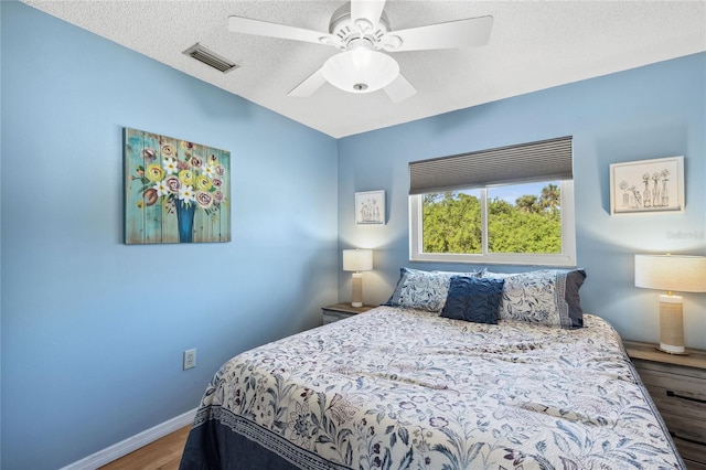 bedroom with ceiling fan, wood-type flooring, and a textured ceiling