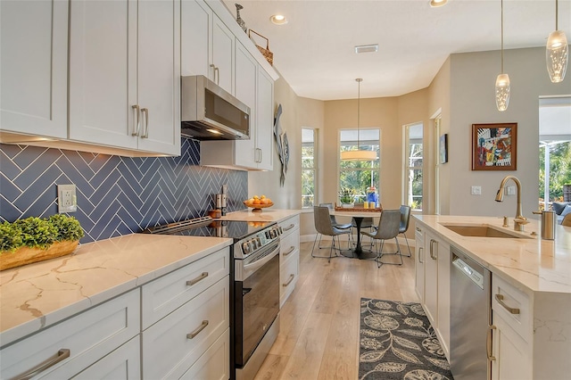 kitchen with sink, white cabinets, hanging light fixtures, light stone counters, and stainless steel appliances