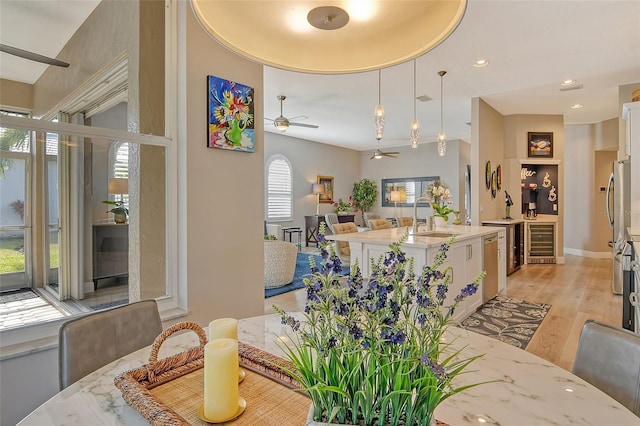 dining space featuring wine cooler, sink, light hardwood / wood-style floors, and ceiling fan