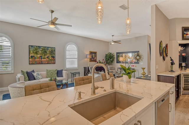 kitchen featuring sink, hanging light fixtures, stainless steel dishwasher, ceiling fan, and light stone counters