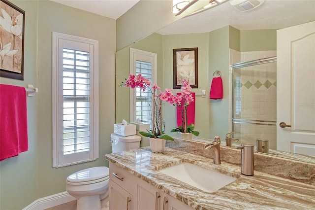 bathroom with vanity, a shower with door, toilet, and a healthy amount of sunlight