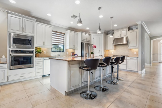 kitchen with decorative light fixtures, light tile patterned floors, stainless steel appliances, light stone countertops, and a center island with sink