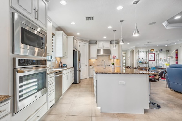 kitchen with an island with sink, dark stone countertops, white cabinets, hanging light fixtures, and stainless steel appliances