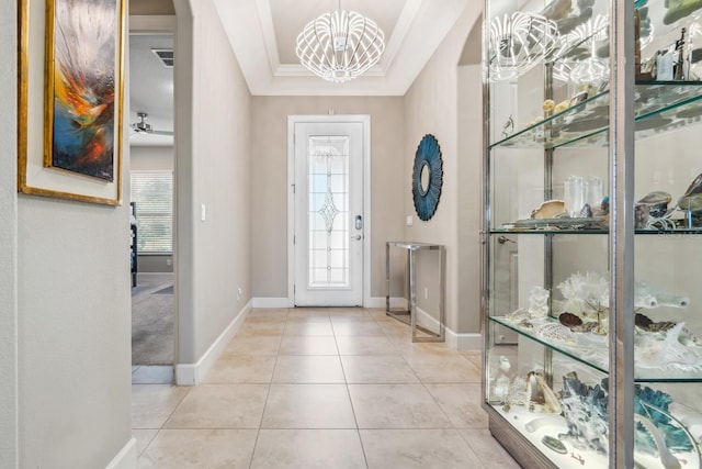 entrance foyer featuring an inviting chandelier, ornamental molding, a raised ceiling, and light tile patterned floors