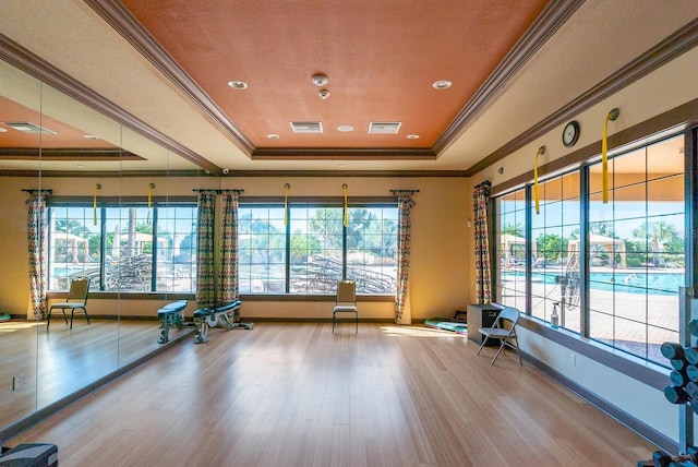 exercise area with crown molding, a raised ceiling, and light wood-type flooring