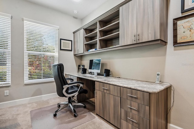 home office with baseboards, built in desk, and light colored carpet