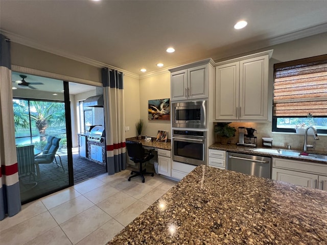 kitchen with white cabinets, a sink, stainless steel appliances, crown molding, and built in desk