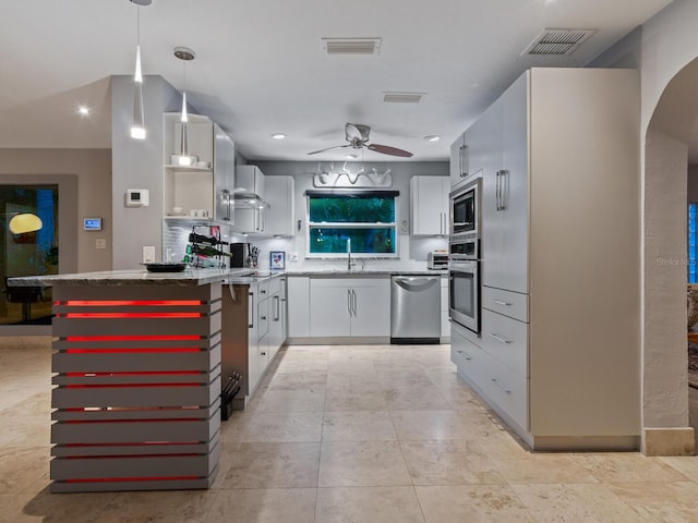 kitchen featuring arched walkways, appliances with stainless steel finishes, wall chimney range hood, and visible vents