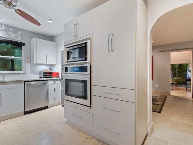 kitchen featuring white cabinets, a ceiling fan, decorative backsplash, light stone countertops, and stainless steel appliances