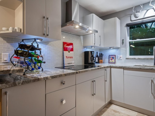 kitchen featuring decorative backsplash, wall chimney exhaust hood, light stone counters, black electric stovetop, and a sink