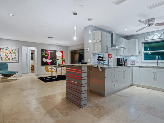 kitchen with a peninsula, a sink, white cabinetry, decorative backsplash, and wall chimney exhaust hood