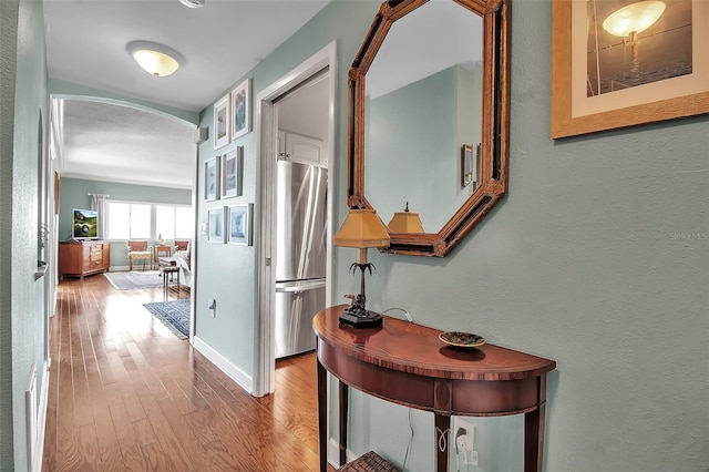 hallway featuring arched walkways, a textured wall, baseboards, and wood finished floors