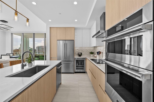 kitchen featuring wine cooler, stainless steel appliances, a sink, wall chimney range hood, and modern cabinets