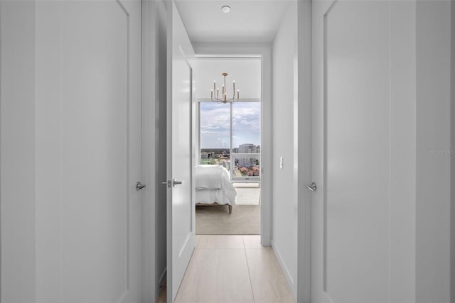 hall with light tile patterned floors, a chandelier, and baseboards